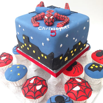 spiderman birthday cake on a cake stand with cupcakes decorated with spiderman below