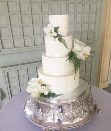 4 tier buttercream wedding cake with polka dots and striped pattern decorated with orchids and ferns