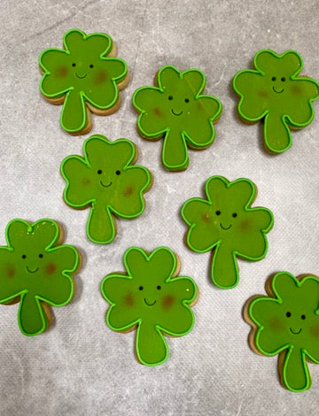 Green clover-shaped cookies with smiling faces for St Patrick's Day Celebrations