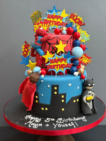 Superhero-themed birthday cake with Spider-Man, Batman, and other characters on a gray background.