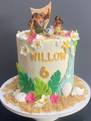 Tall buttercream covered cake decorated with Moana and flowers, shells and leaves