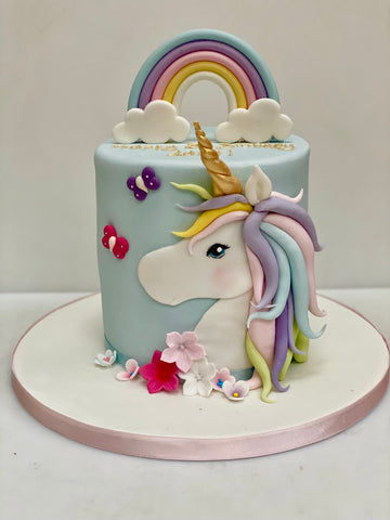 Tall pale blue rainbow cake with a unicorn head on the side of the cake and a rainbow on top