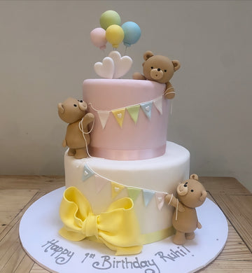Cute cake showing sugar teddy bears hanging some bunting around the cake