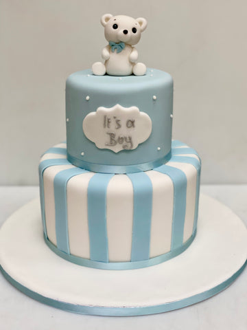 Two-tiered baby shower cake with a teddy bear and 'It's a Boy' sign on a white background