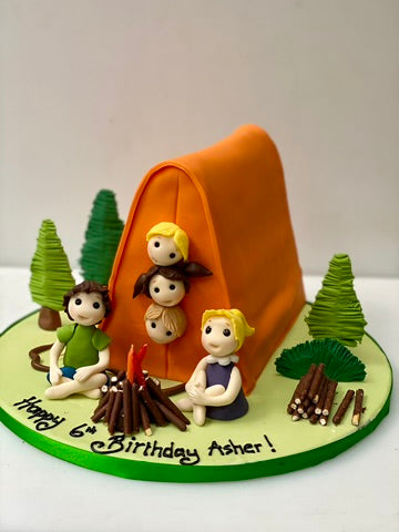 Birthday cake with camping theme featuring children around a campfire and tent.