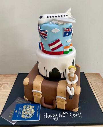 Travel-themed birthday cake with airplane, flags, suitcase, and figurine on a black base.