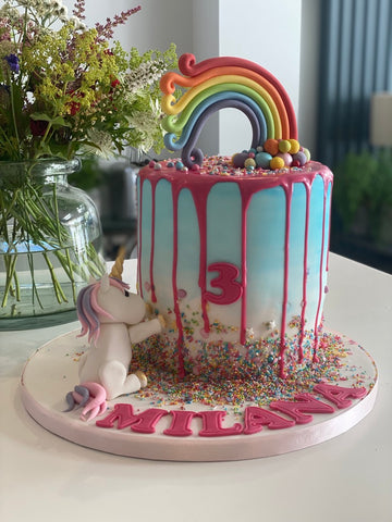 Rainbow drip cake with a sugar unicorn eating it at the bottom
