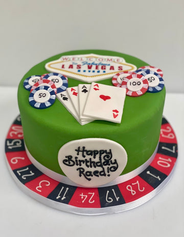 Green birthday cake with Las Vegas-themed decorations including poker chips, cards, and roulette elements.