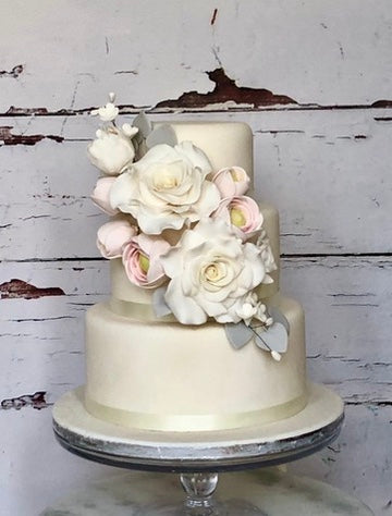 3 tiered wedding cake with sugar roses and ranunculars across the front of the cake, delivered across london