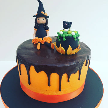 Witch and Cauldron Orange Drip Halloween-themed cake with witch figurine and black cat on a white background