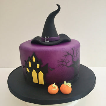 Halloween-themed cake with a witch's hat, pumpkins, and haunted house on a white background