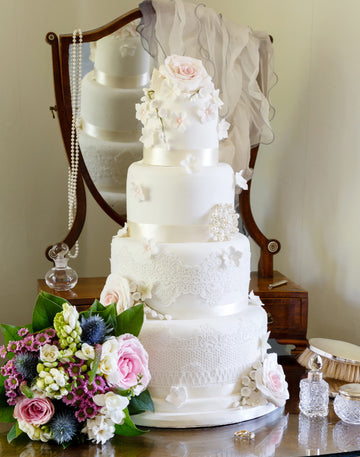 four tier wedding cake decorated with edible lace, pink and white sugar flowers and a brooch all delivered to london