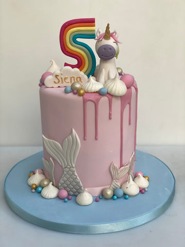 Tall pink drip cake with a unicorn on top and a mermaid tail on the base