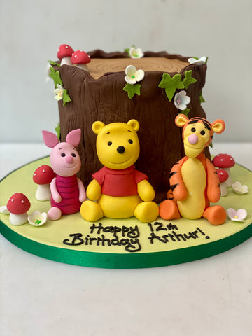 Birthday cake shaped like a log with winnie the pooh, tigger and piglet in front of it. Cake made in London