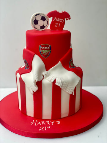 Two-tiered birthday cake with Arsenal football club design, including a jersey and football on top.