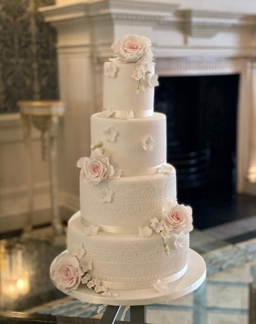 4 tiered wedding cake decorated with pink sugar roses and edible lace