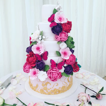 5 tier wedding cake wit vibrant swathes of sugar flowers and butterflies and gold detailing on the bottom tier delivered in london