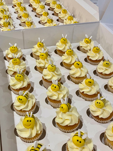 Cupcakes decorated with yellow frosting and bee-themed decorations on a white tray.