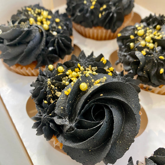 Cupcakes with black frosting and gold sprinkles on a white plate.