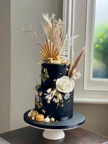 Decorative cake with gold shells, white flowers, and dried herbs on a stand.