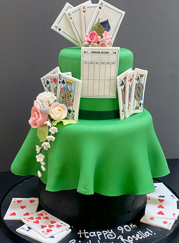 2 tier Green cake with playing cards and a scoreboard on top, surrounded by cards and flowers