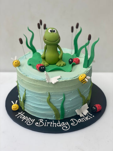 Buttercream Frog birthday Cake - sugar frog sat in a cake decorated. ton look like a pond with icing reeds and an ombre colouring.  Little icing bees and ladybirds. on the sides to decorate