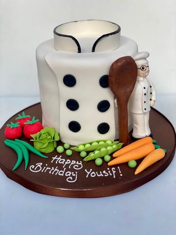 Cake shaped like a chef's jacket with kitchen-themed decorations on a white background