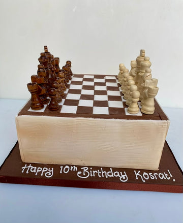 Chess-themed birthday cake with wooden pieces on a checkered board, featuring 'Happy 10th Birthday Kosrat!' text.