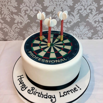 Birthday cake with dartboard design and candles, against a decorative wall.