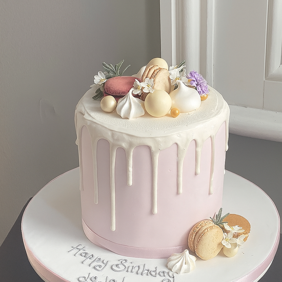 Pink drip cake with macarons, meringue kisses and chocolates to decorate