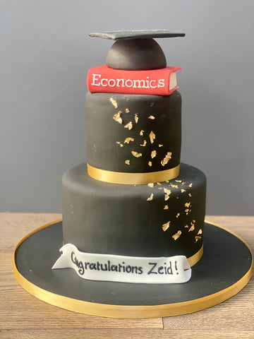Graduation-themed cake with economics book and mortarboard on a gray background