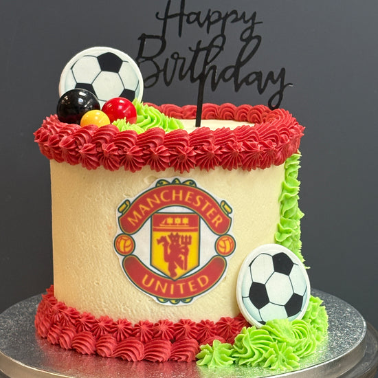Birthday cake with Manchester United logo and soccer ball decorations on a black background for london delivery