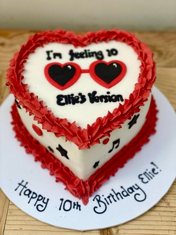 Heart-shaped birthday cake with red and white frosting, featuring sunglasses for Taylor Swift