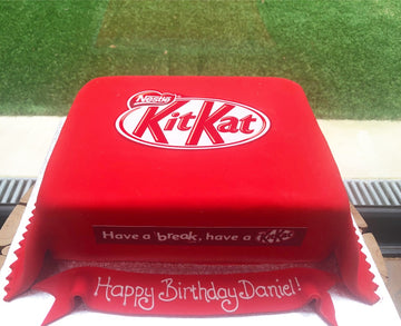 Red KitKat bar-shaped cake with 'Happy Birthday Daniel!' message on a grassy background
