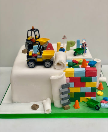 Lego city birthday cake with lego bricks making up the sides, lego trucks on top and lego construction figures