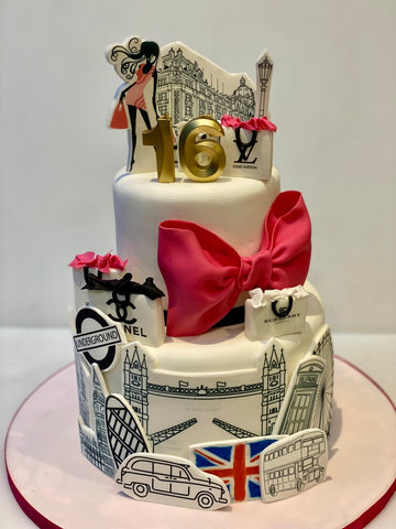 Decorative cake with London-themed elements, shopping bags, a stylish woman and a large pink bow on a white background