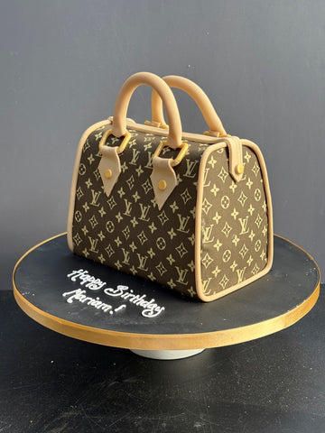 Cake shaped like a Louis Vuitton handbag with monogram pattern on a black stand