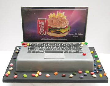 MAC Laptop-shaped birthday cake with a screen displaying a burger and Coca-Cola can, surrounded by colorful candies.