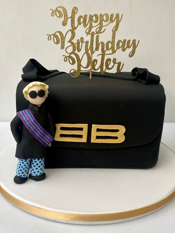 Black cake shaped like a handbag with a figurine and 'Happy Birthday Peter' topper.