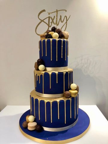 3 tiered navy cake with gold drip and decorated with chocolates, macarons and meringues