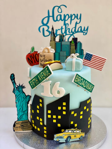 Birthday cake with New York City-themed decorations including the Statue of Liberty, taxi, and American flag.