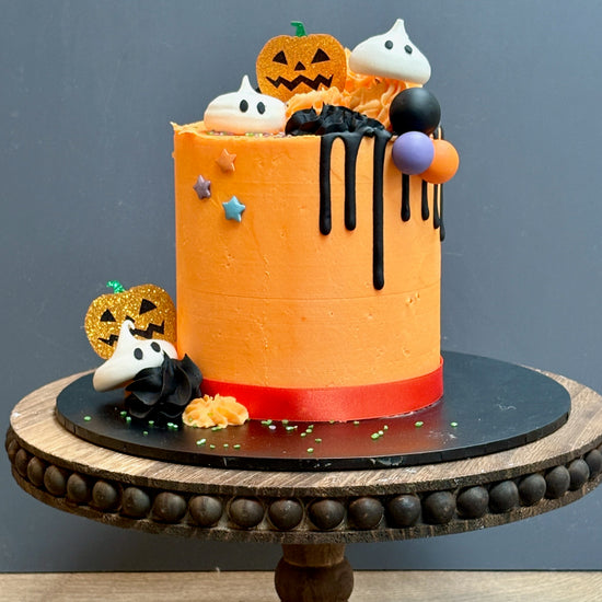 Halloween themed cake with meringue ghost decorations, a black drip, sparkly pumpkins and halloween balls