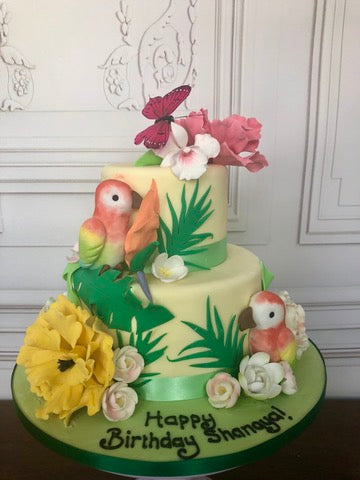 Birthday cake decorated with sugar parrots and exotic leaves and flowers