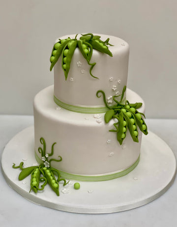 Two-tiered cake decorated with green peas and ribbons on a white background