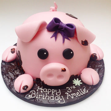 Pink pig birthday cake with a purple bow sitting in lots of chocolate mud