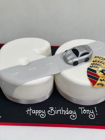 Model of a Porsche car on a road on a cake with a birthday message on a white background