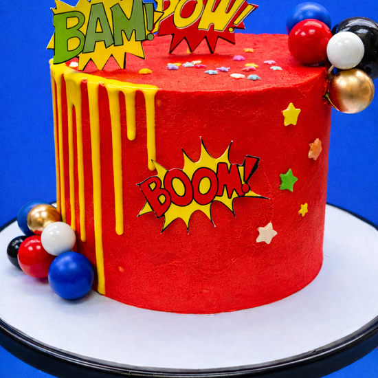 red super hero kids birthday cake with comic book exclamations to decorate delivered in london