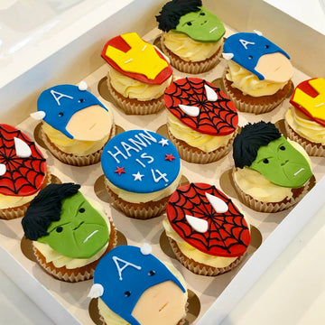Cupcakes decorated with superhero-themed toppers including hulk, spiderman, ironman, captain america 