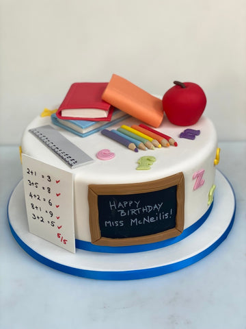 Teacher-themed birthday cake with books, apple, and chalkboard