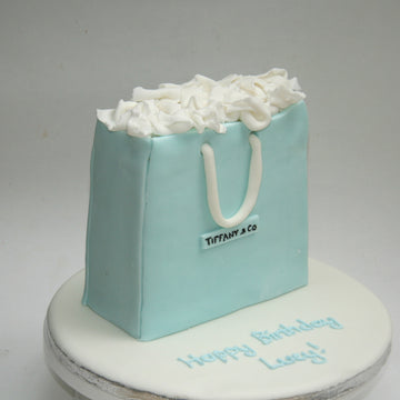 Cake designed like a Tiffany & Co. shopping bag with white ruffles on a gray background